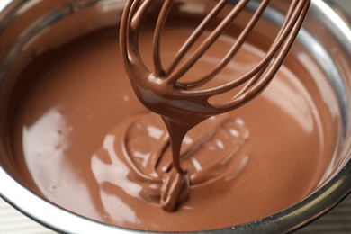 Photo of Chocolate dough dripping from whisk into bowl on table, closeup