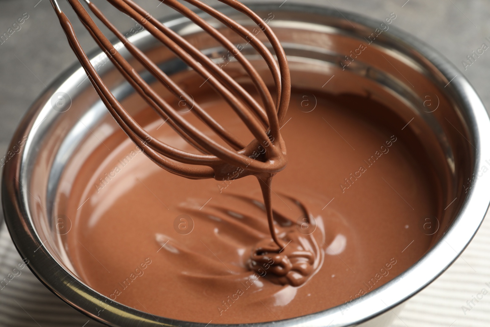 Photo of Chocolate dough dripping from whisk into bowl on table, closeup