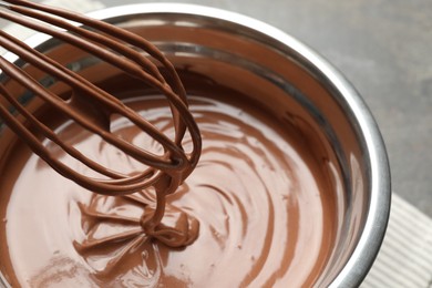 Photo of Chocolate dough dripping from whisk into bowl on table, closeup