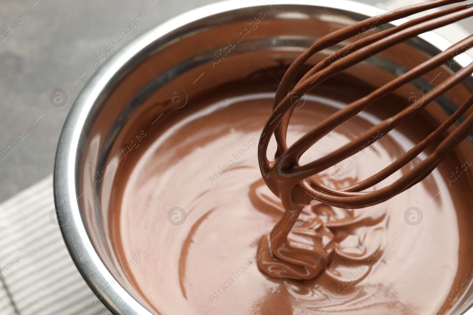 Photo of Chocolate dough dripping from whisk into bowl on table, closeup