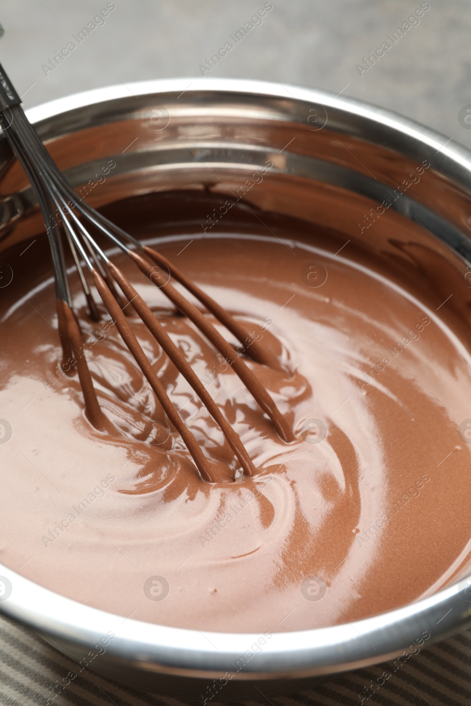 Photo of Chocolate dough and whisk in bowl on grey table, closeup