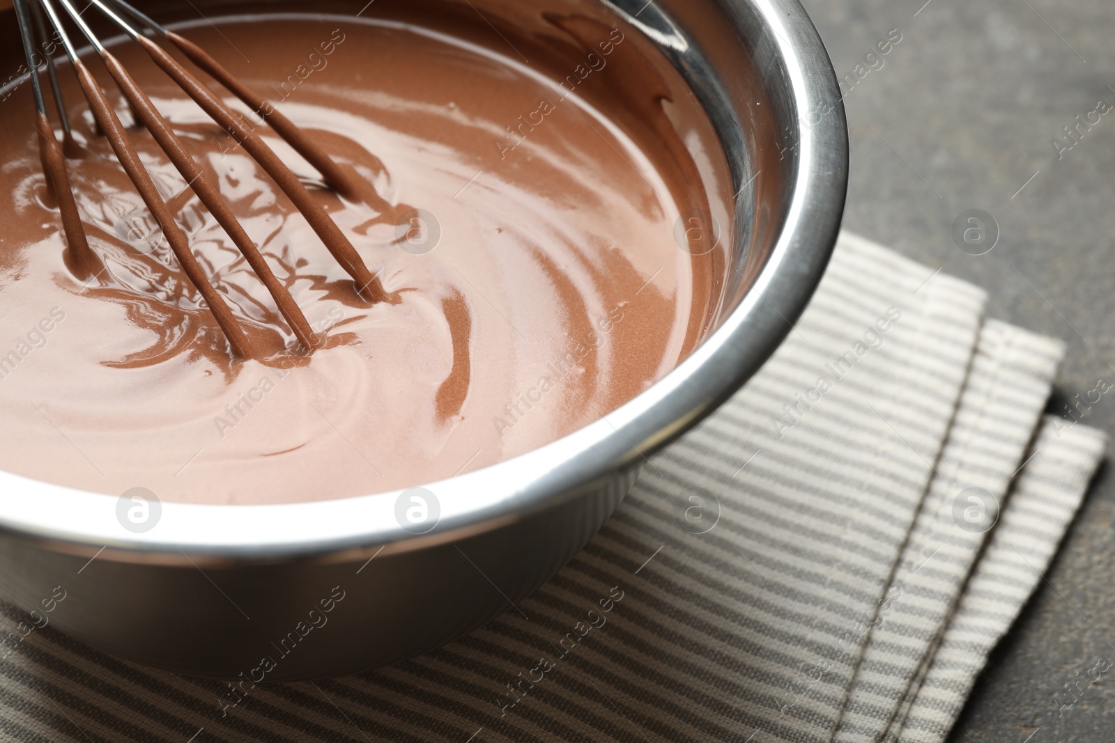 Photo of Chocolate dough and whisk in bowl on grey table, closeup