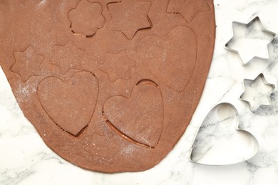 Photo of Chocolate dough and cookie cutters on white marble table, flat lay