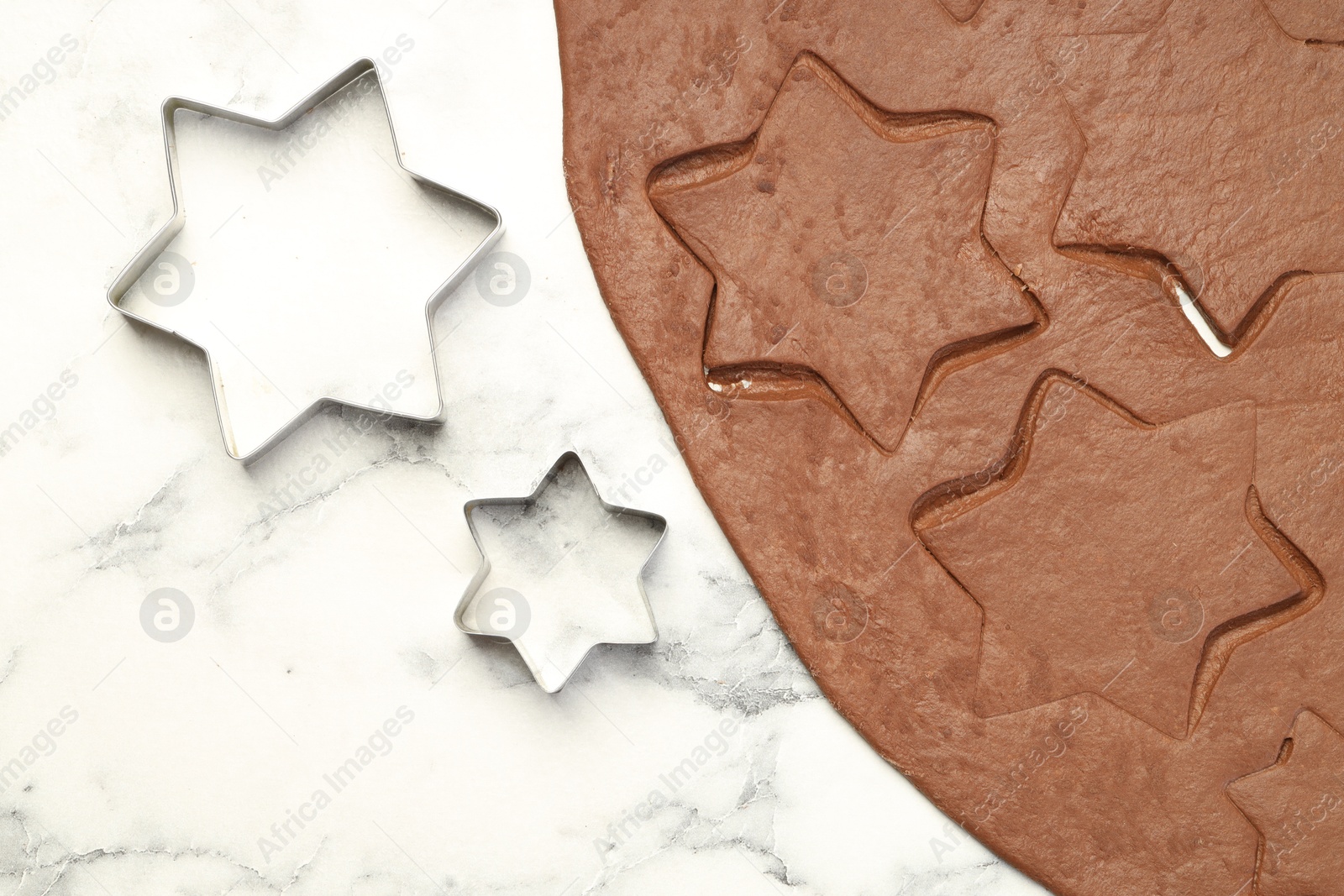 Photo of Chocolate dough and cookie cutters on white marble table, flat lay