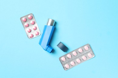 Photo of Asthma inhaler and pills on light blue background, flat lay