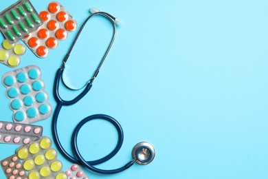 Photo of Stethoscope and pills on light blue background, flat lay. Space for text