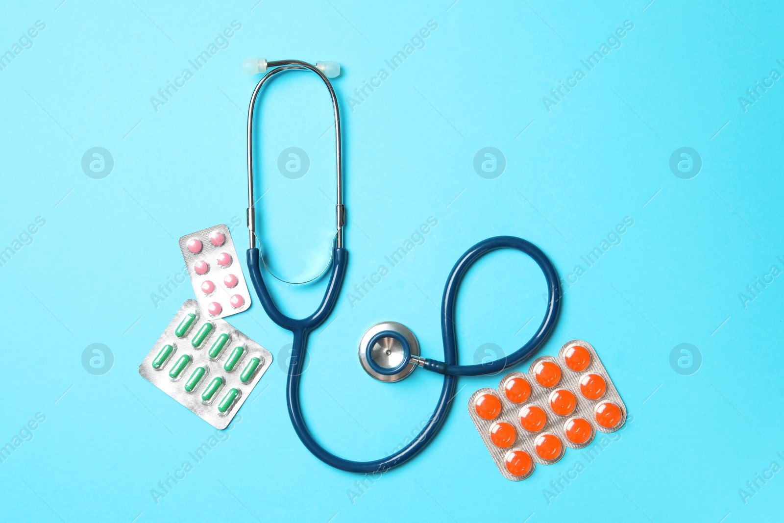 Photo of Stethoscope and pills on light blue background, flat lay