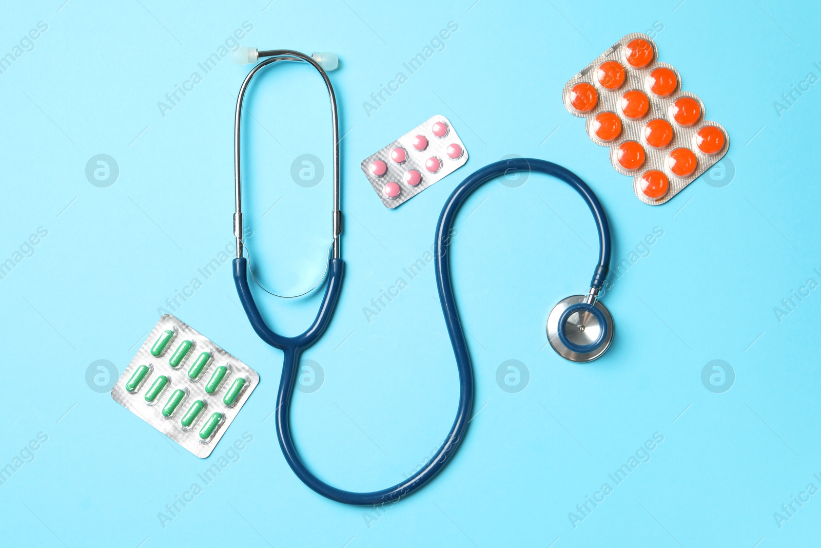 Photo of Stethoscope and pills on light blue background, flat lay