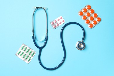 Photo of Stethoscope and pills on light blue background, flat lay