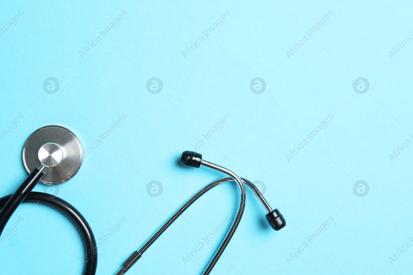 Photo of Stethoscope on light blue background, top view. Space for text