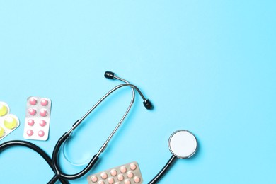 Photo of Stethoscope and pills on light blue background, flat lay. Space for text