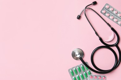 Photo of Stethoscope and pills on pink background, flat lay. Space for text