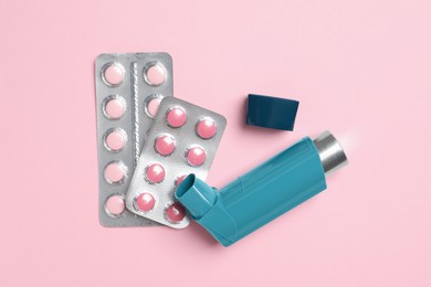 Photo of Asthma inhaler and pills on pink background, flat lay