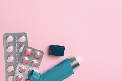 Photo of Asthma inhaler and pills on pink background, flat lay. Space for text