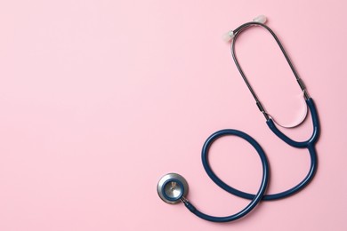 Photo of Stethoscope on pink background, top view. Space for text