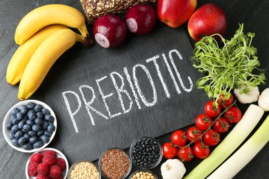 Photo of Slate board with word Prebiotic and different fresh products on black table, flat lay