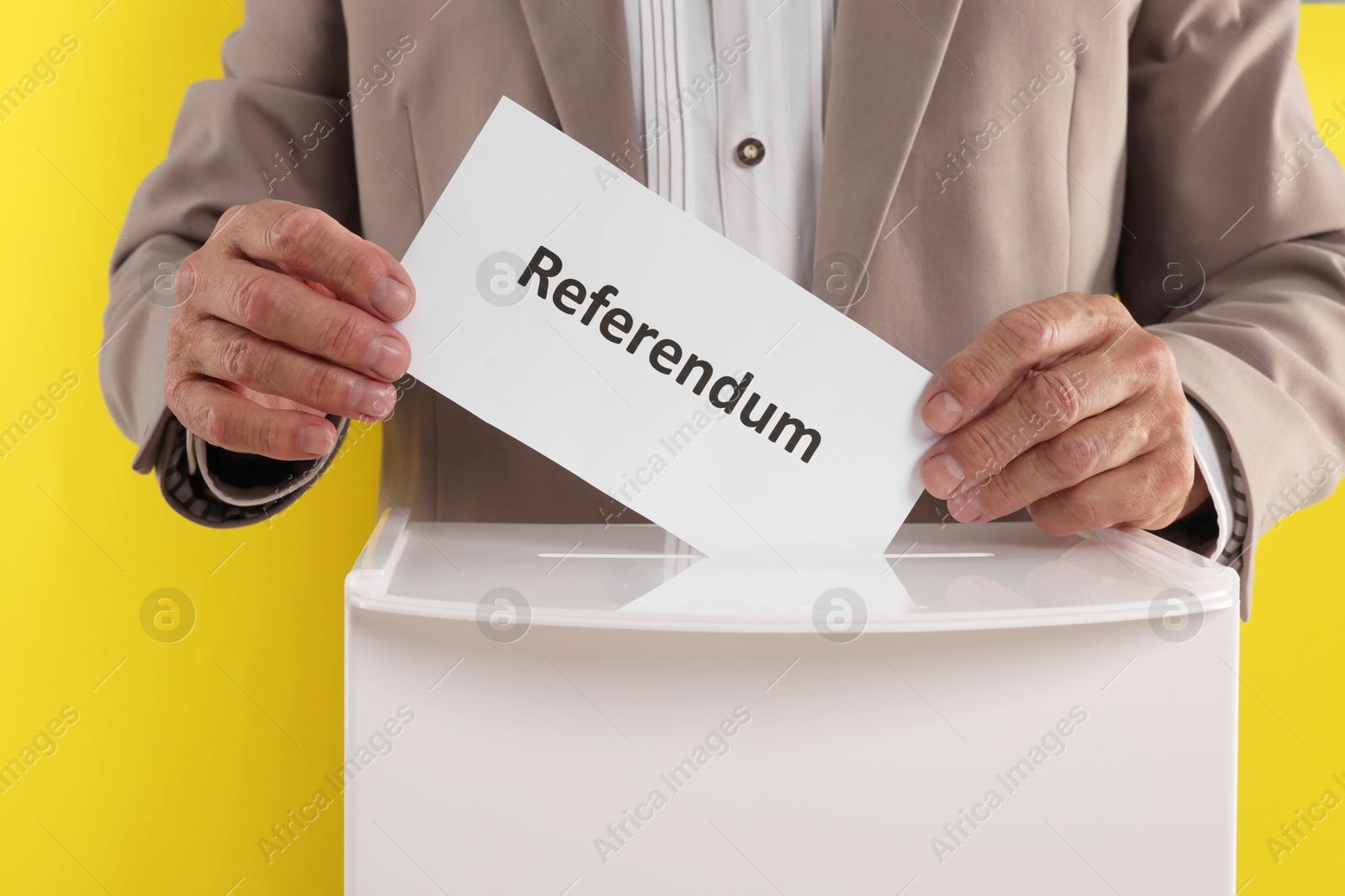 Photo of Referendum. Man putting his vote into ballot box against yellow background, closeup