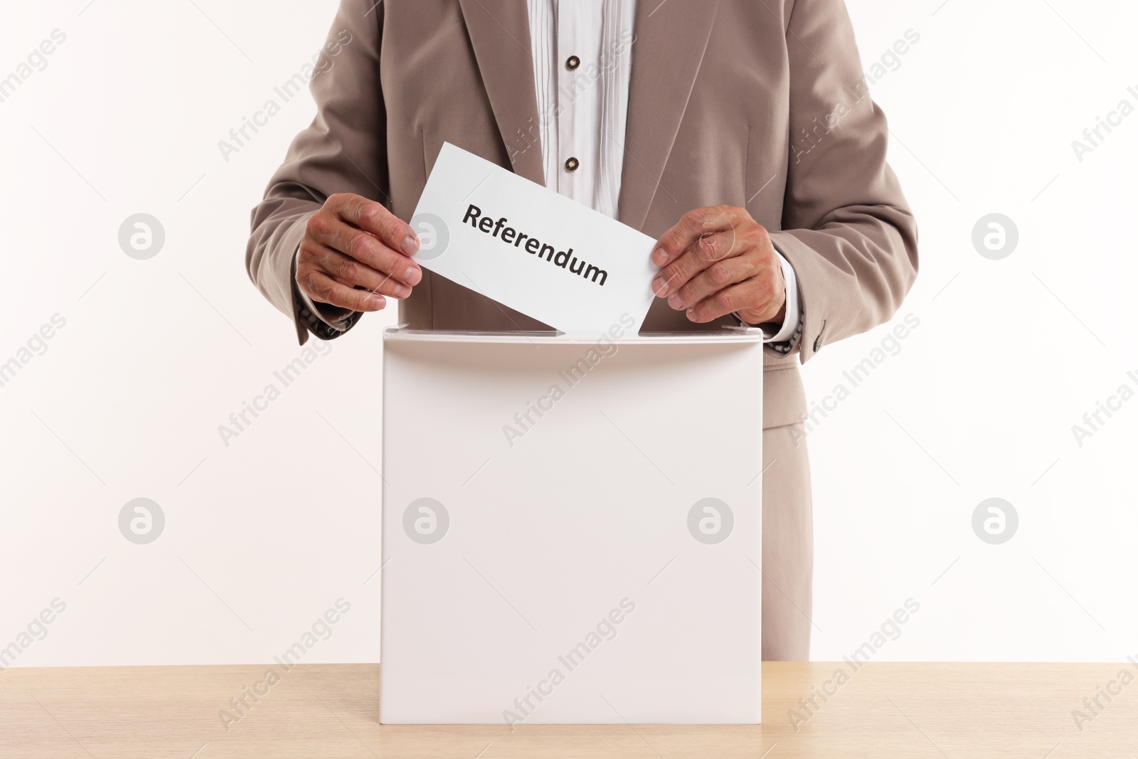 Photo of Referendum. Man putting his vote into ballot box at wooden table against white background, closeup