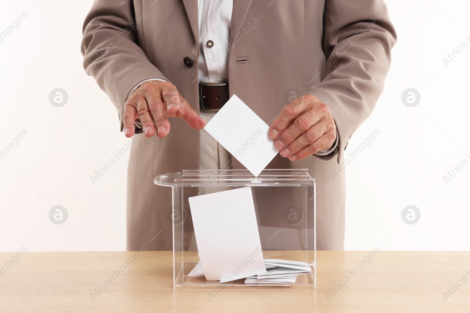 Photo of Referendum. Man putting his vote into ballot box at wooden table against white background, closeup