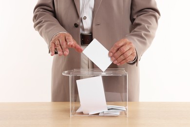 Photo of Referendum. Man putting his vote into ballot box at wooden table against white background, closeup