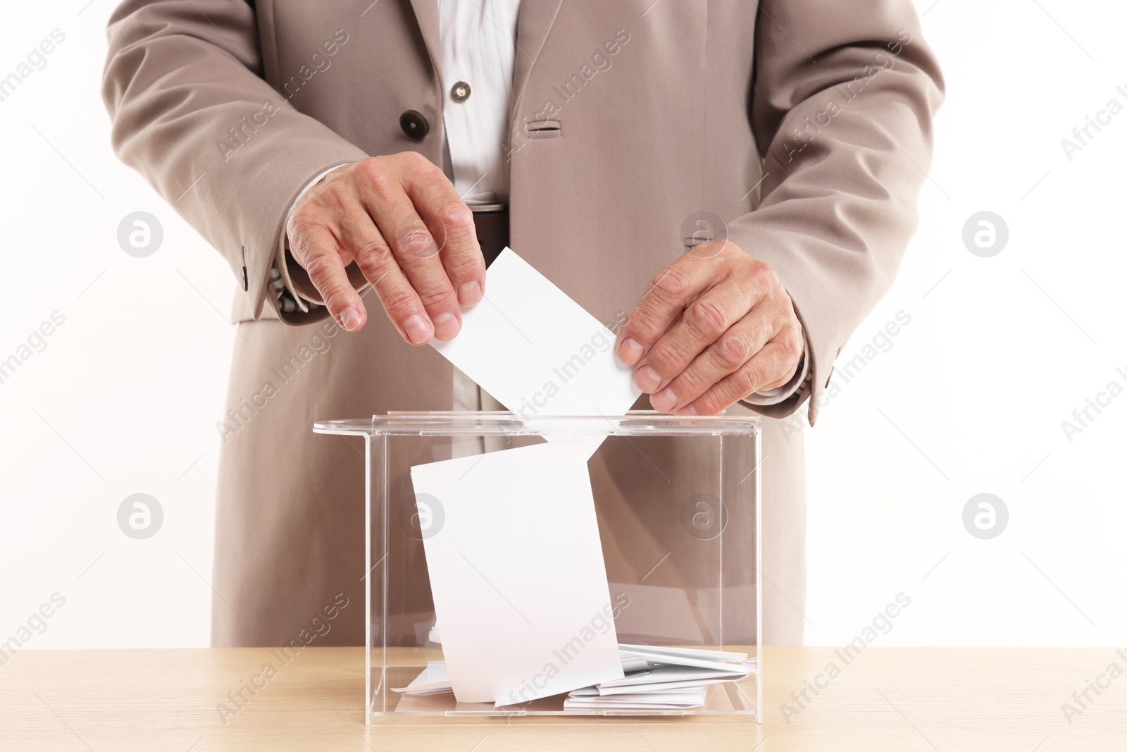 Photo of Referendum. Man putting his vote into ballot box at wooden table against white background, closeup