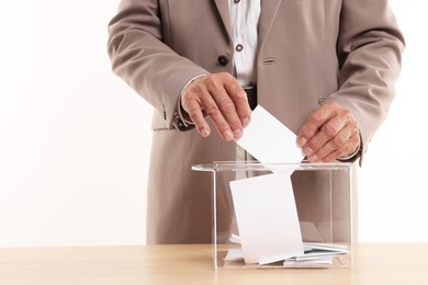 Referendum. Man putting his vote into ballot box at wooden table against white background, closeup