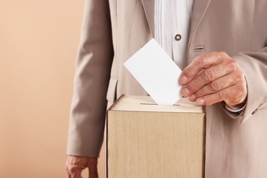 Referendum. Man putting his vote into ballot box against beige background, closeup