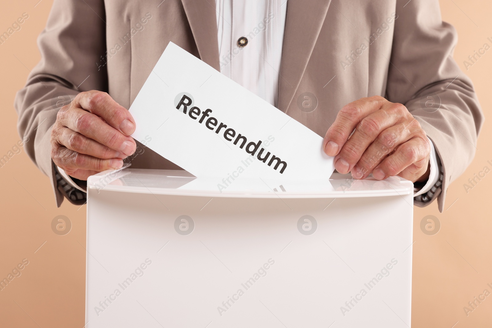 Photo of Referendum. Man putting his vote into ballot box against beige background, closeup