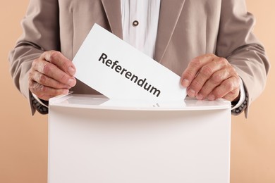 Referendum. Man putting his vote into ballot box against beige background, closeup