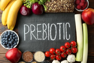 Slate board with word Prebiotic and different fresh products on wooden table, flat lay