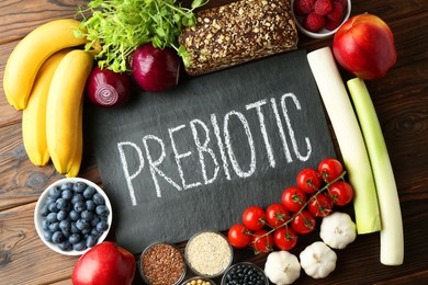 Slate board with word Prebiotic and different fresh products on wooden table, flat lay