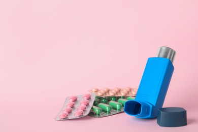 Photo of Inhaler and pills on pink background, closeup with space for text. Asthma treatment