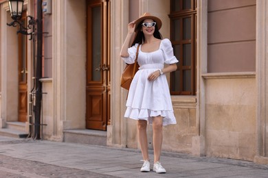 Smiling woman in stylish hat and sunglasses on city street