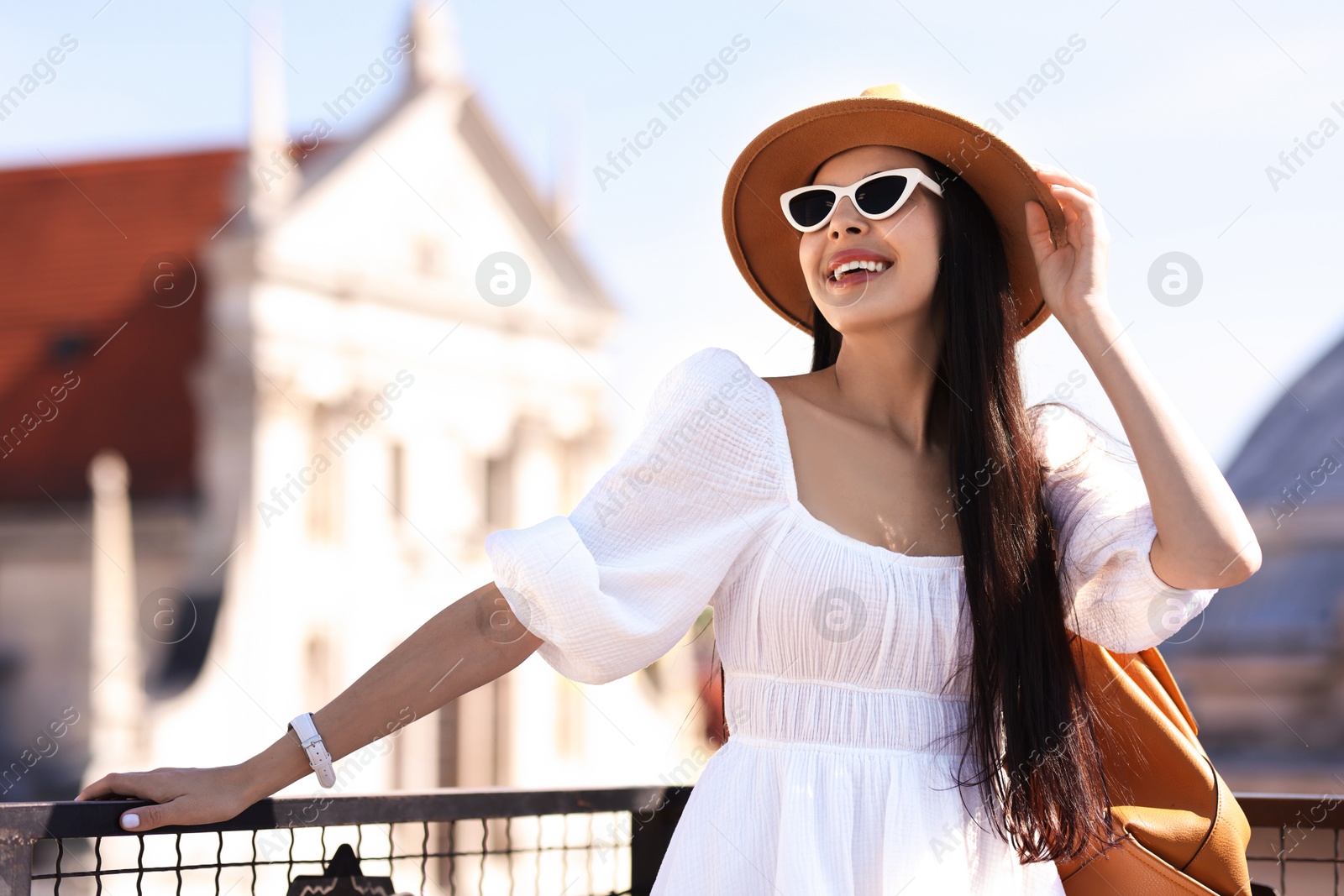 Photo of Smiling woman in stylish hat and sunglasses with backpack on city street