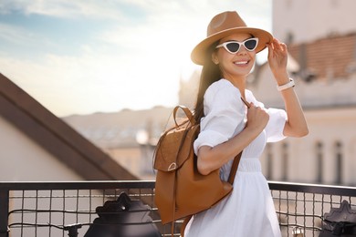 Smiling woman in stylish hat and sunglasses with backpack on city street