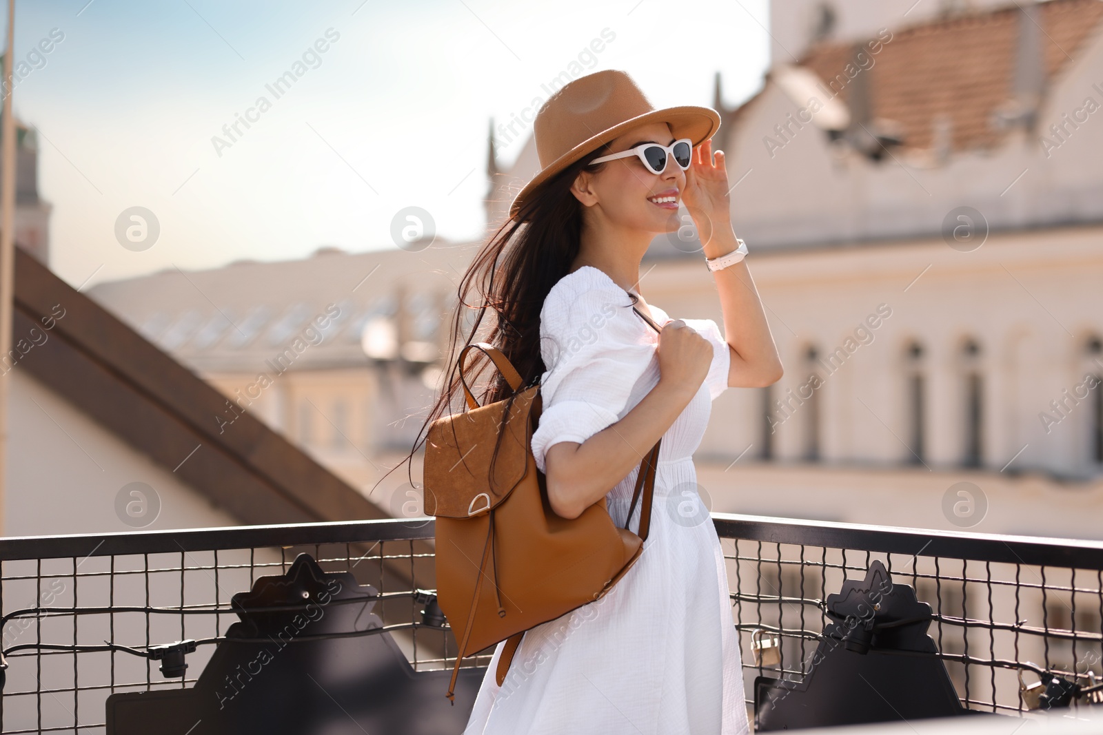 Photo of Smiling woman in stylish hat and sunglasses with backpack on city street