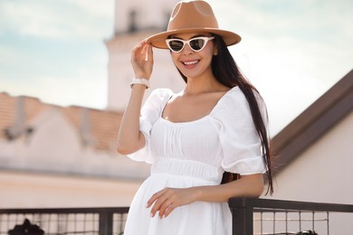 Smiling woman in stylish hat and sunglasses on city street