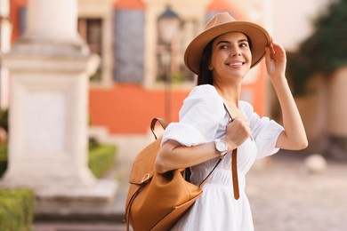 Photo of Beautiful young woman in stylish hat with backpack on city street, space for text