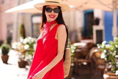 Smiling young woman in stylish hat and sunglasses on city street