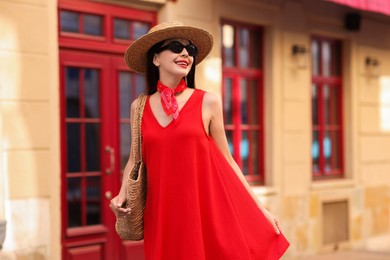 Smiling young woman in stylish hat and sunglasses on city street