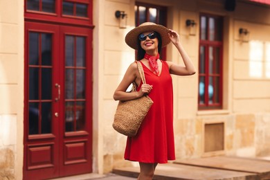 Photo of Smiling young woman in stylish hat and sunglasses on city street