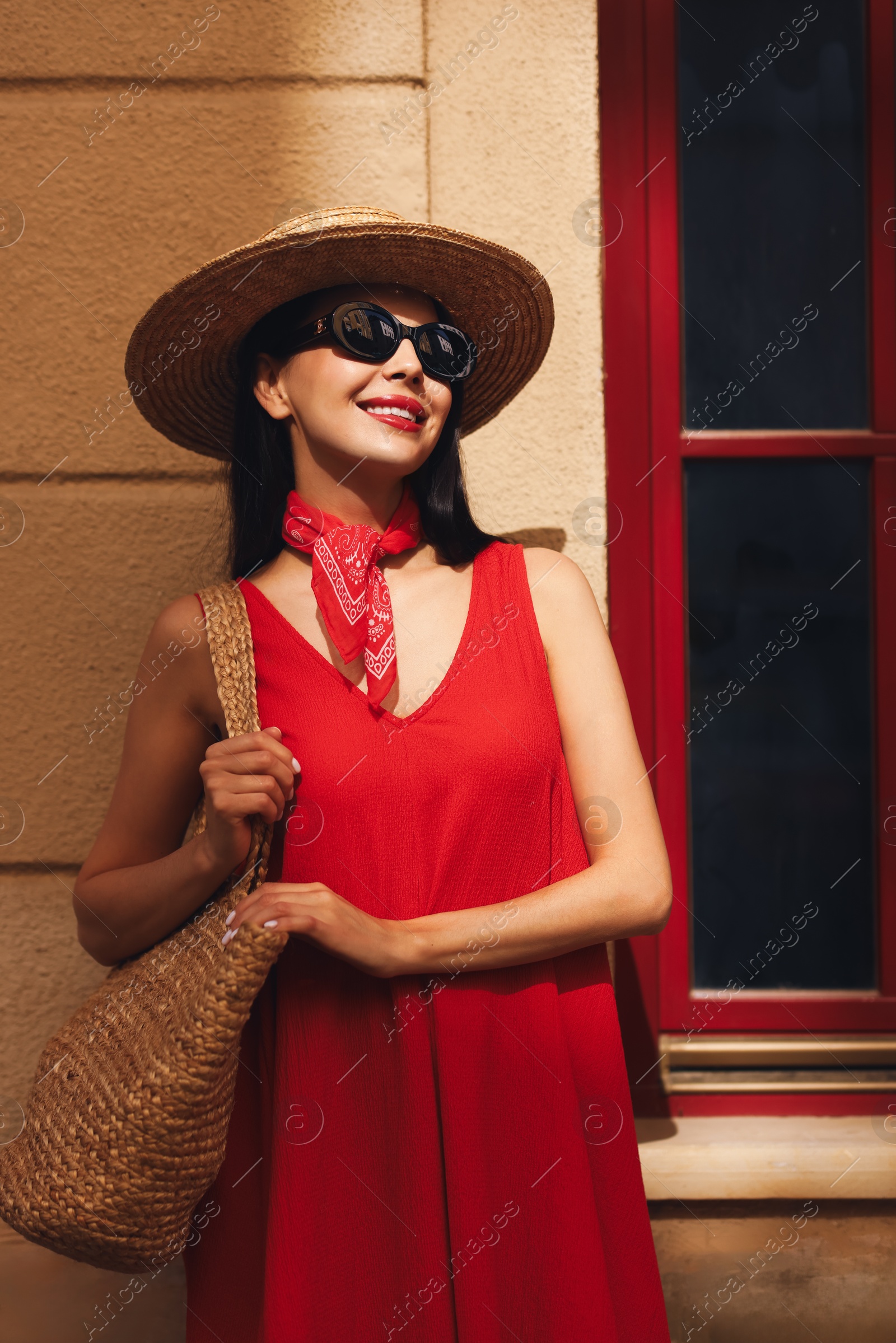 Photo of Smiling young woman in stylish hat and sunglasses near building outdoors