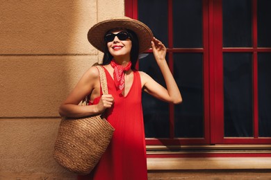 Smiling young woman in stylish hat and sunglasses near building outdoors