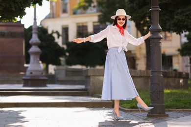 Smiling young woman in stylish hat and sunglasses on city street, space for text