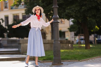 Photo of Smiling young woman in stylish hat and sunglasses on city street, space for text