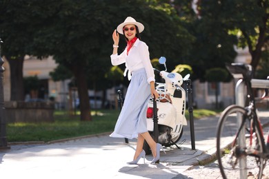 Photo of Smiling young woman in stylish hat and sunglasses on city street