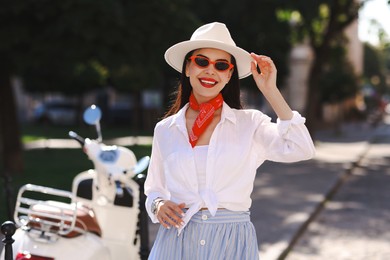 Photo of Smiling young woman in stylish hat and sunglasses on city street