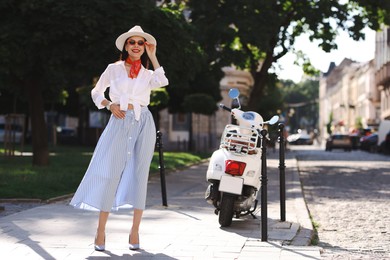 Smiling young woman in stylish hat and sunglasses on city street