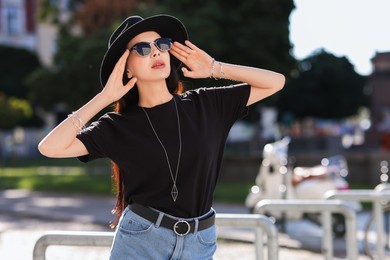 Photo of Young woman in stylish black hat and sunglasses on city street