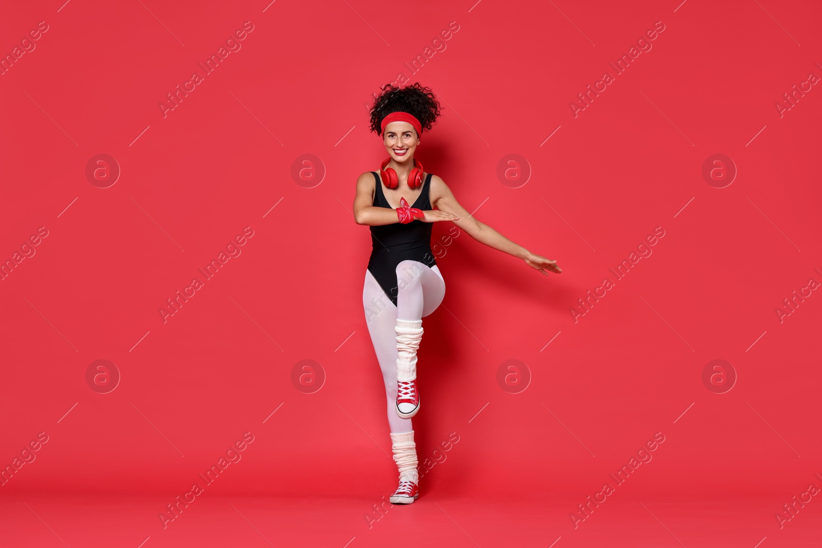 Photo of Woman with headphones doing aerobic exercise on red background